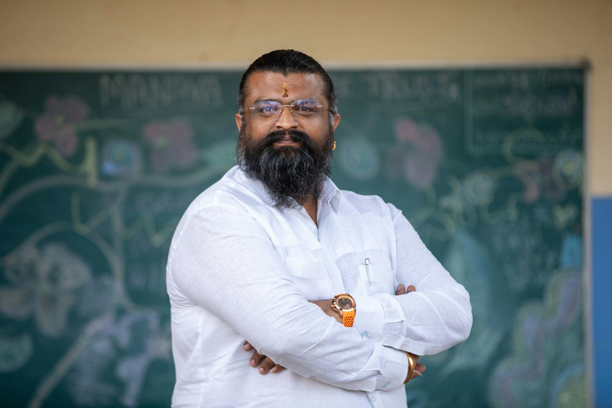 A confident man with folded arms stands in front of a chalk-drawn blackboard.